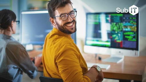 Smiling man coding on computer screens.